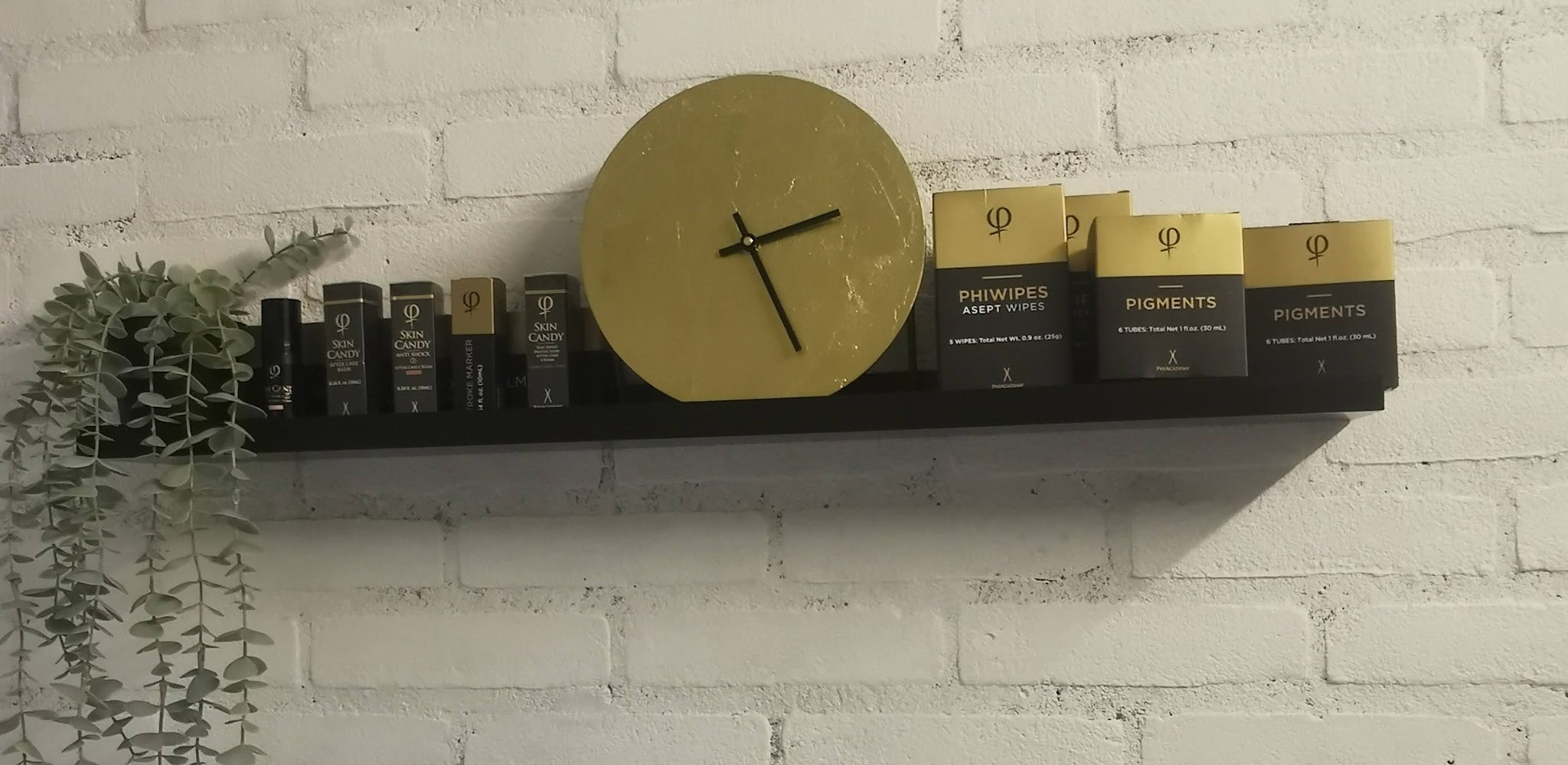 De studio: een zwarte plank met een gouden klok en producten tegen een witte bakstenen muur
